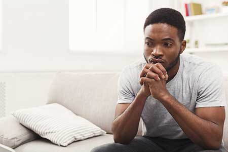An African American man sitting on a couch thinking how he can get involved in the adoption process