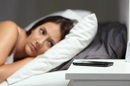 woman lies in bed looking at her cell phone on table and worries