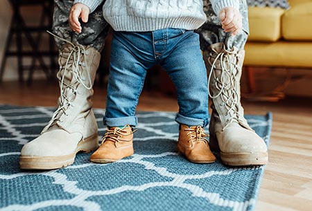 Toddler standing between his adoptive military dad's boots