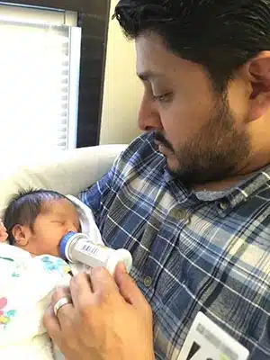 A new adoptive father lovingly holding and feeding a bottle to his adopted infant