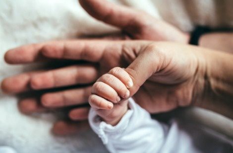 A family created by adopting after infertility: father's hand, mother's hand, and baby clutching mother's thumb