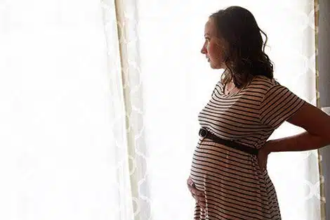 Pregnant woman standing in front of a window holding her belly