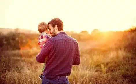 Dad holding his toddler son in a field at sunset