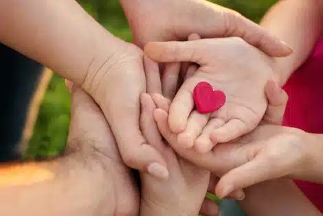 Adult and child hands holding a small red paper heart