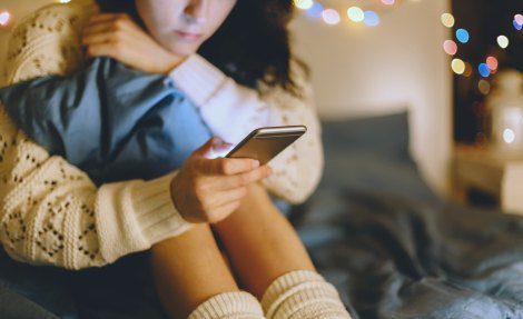 Young woman looking at her cell phone while seated on her bed