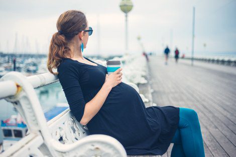 pregnant woman sits on a pier as she thinks about if adoption vs parenting will be the best choice