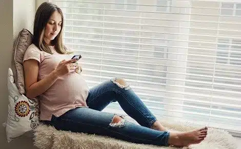 Pregnant woman at home, texting on her phone