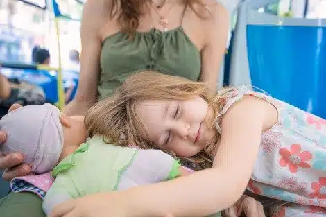A mom rides on a city bus with her sleeping daughter