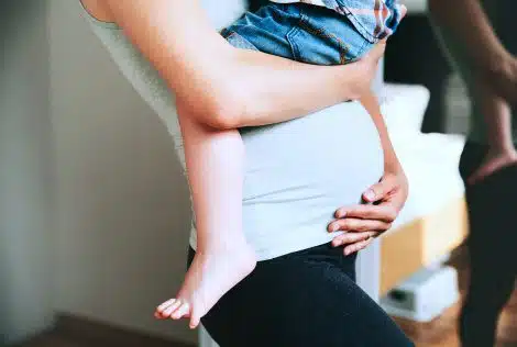 Pregnant woman cradles her belly while holding her toddler