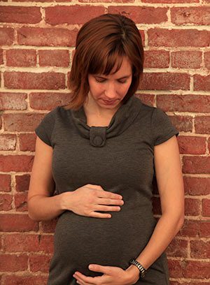 Pregnant woman leaning against brick wall