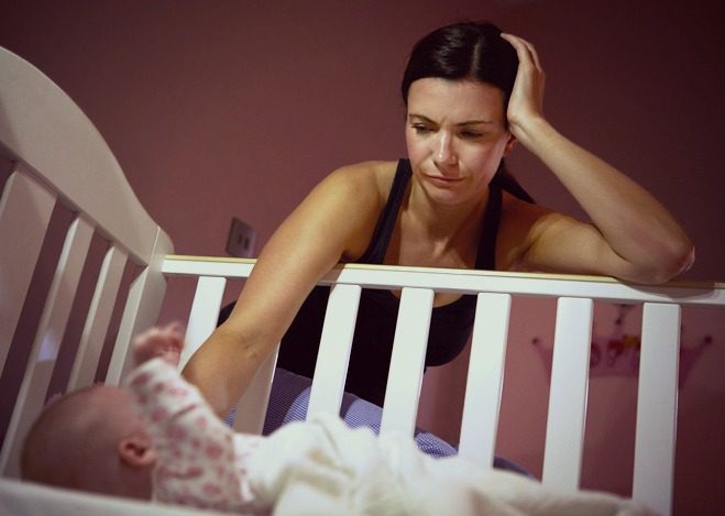 Anxious and depressed new adoptive mother gazes at baby in her crib