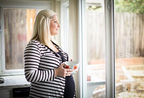 Pregnant woman deep in thought looks out her back patio door