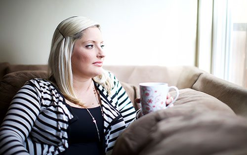 Pregnant woman sits on her sofa thinking about adoption