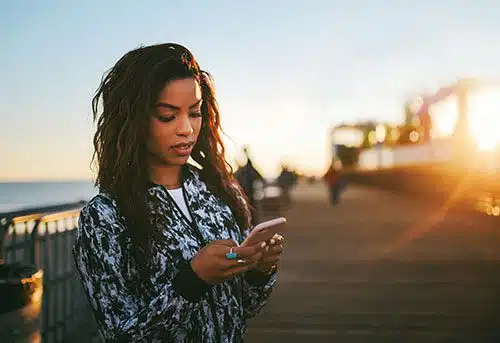 Woman standing on a pier texts with her son's adoptive mom