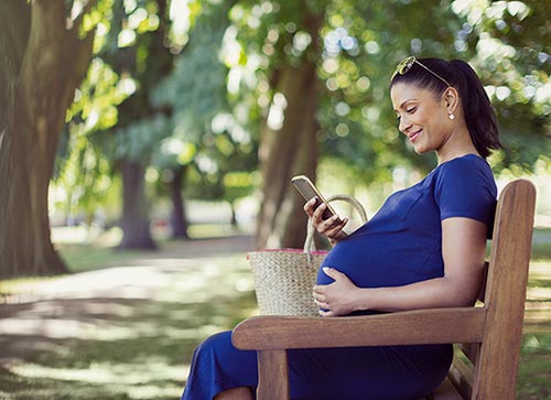 Pregnant woman sitting on a park bench looking at her cell phone