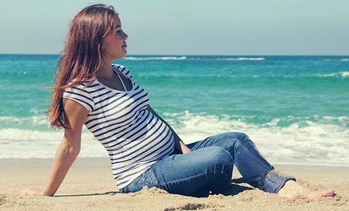 Young woman sitting at a beach, thinking about putting baby up for adoption
