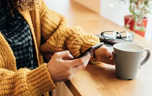 Woman drinking coffee from a mug as she looks at her phone