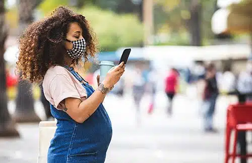 Woman wearing face mask looks online for information about pregnancy and COVID-19