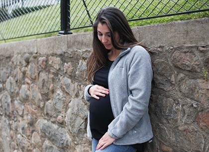 Pregnant woman leaning against an outdoor retaining wall