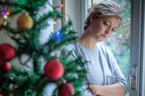 Sad woman by her Christmas tree, thinking, "All I want for Christmas is a baby"