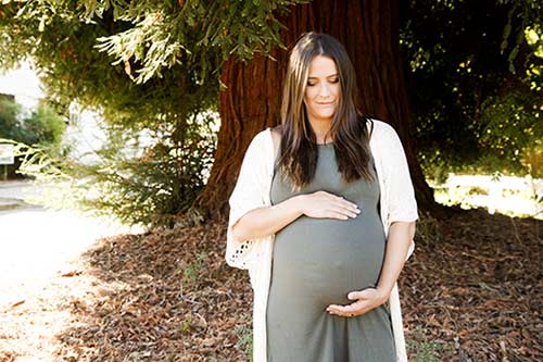 Pregnant woman standing outside, looking down at belly wondering how adoption can benefit her child