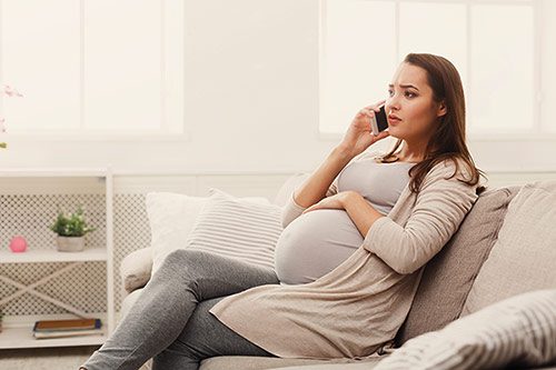 A young pregnant woman talking on her cell phone from her living room
