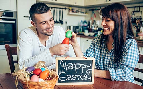 Smiling couple enjoying 1 of the six tips crack open Easter eggs in their kitchen