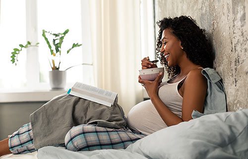 Smiling pregnant woman having breakfast in bed