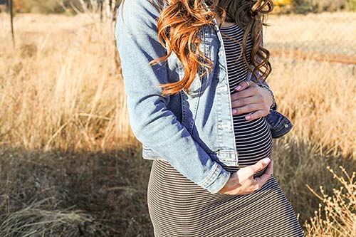 Pregnant woman standing outside in the autumn, cradling her belly