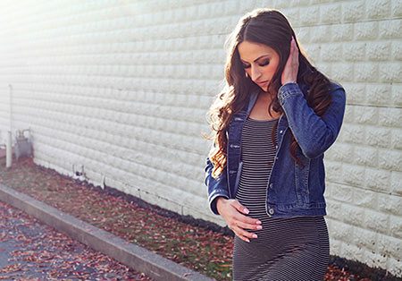 Pregnant woman stands outside, looking at her belly