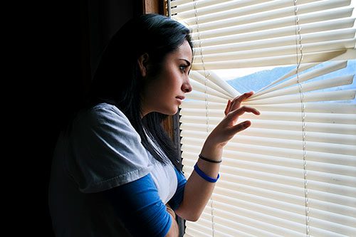 Young woman who is undocumented and pregnant peeks through the window blinds