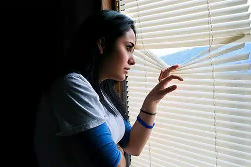 Young woman inmigrante indocumentado and pregnant peeks through the window blinds