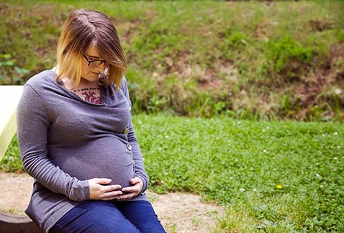Young woman looking down at her pregnant belly at a park