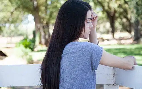 Sad young woman leaning against fence