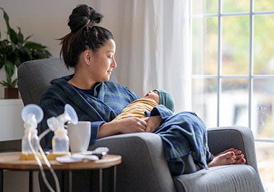 Tired new mother gazes at her baby, breast pump nearby