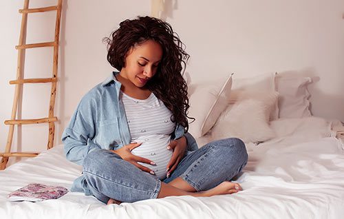 A teen mother-to-be sitting on her bed