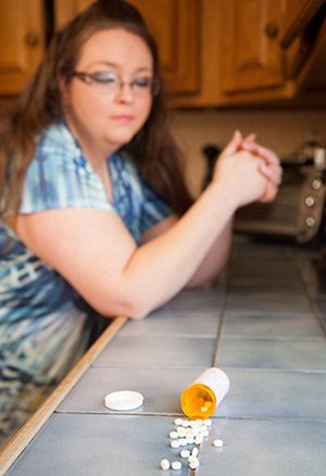Pregnant woman at her kitchen counter, eyeing a bottle of Oxycontin