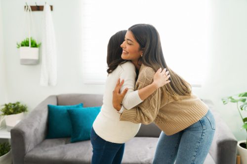 Pregnant woman and her friend hug in the living room