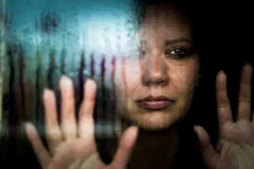 Depressed pregnant woman who is suffering from domestic abuse looking out of a window at the rain