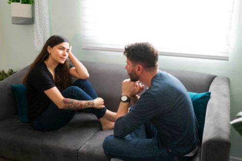 Woman sitting together on the couch with her boyfriend talking about her pregnancy