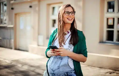 Expectant mother on a city street, looking up from her phone