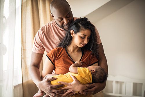 Bi-racial adoptive couple gaze lovingly at their sleeping infant daughter