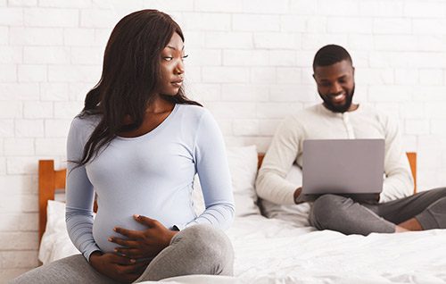 Pregnant woman sitting on her bed, watching her boyfriend for signs of a good father