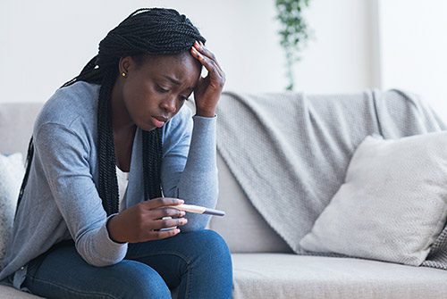 Depressed young woman, holding a positive pregnancy test and dealing with unexpected pregnancy