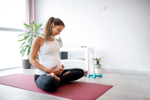 pregnant woman sitting on yoga mat and looking at her belly