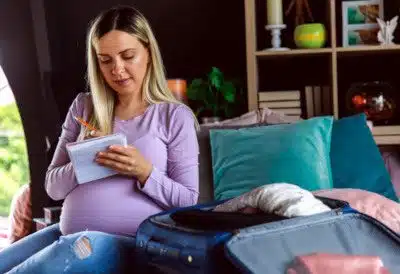 Smiling pregnant woman holding notepad, checking list after she finished packing her hospital bag