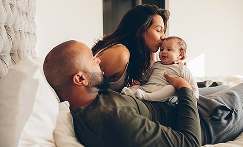 Adoptive parents with their newborn baby boy on the bed