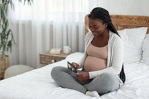 Happy African American pregnant woman sitting on her bed looking at an ultrasound image