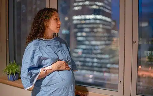 Thoughtful pregnant woman looks out her hospital window