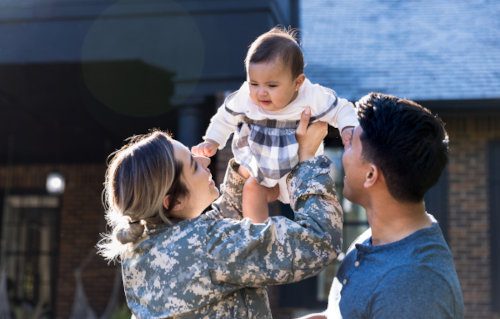  Cheerful female soldier smiles while holding up her baby girl
